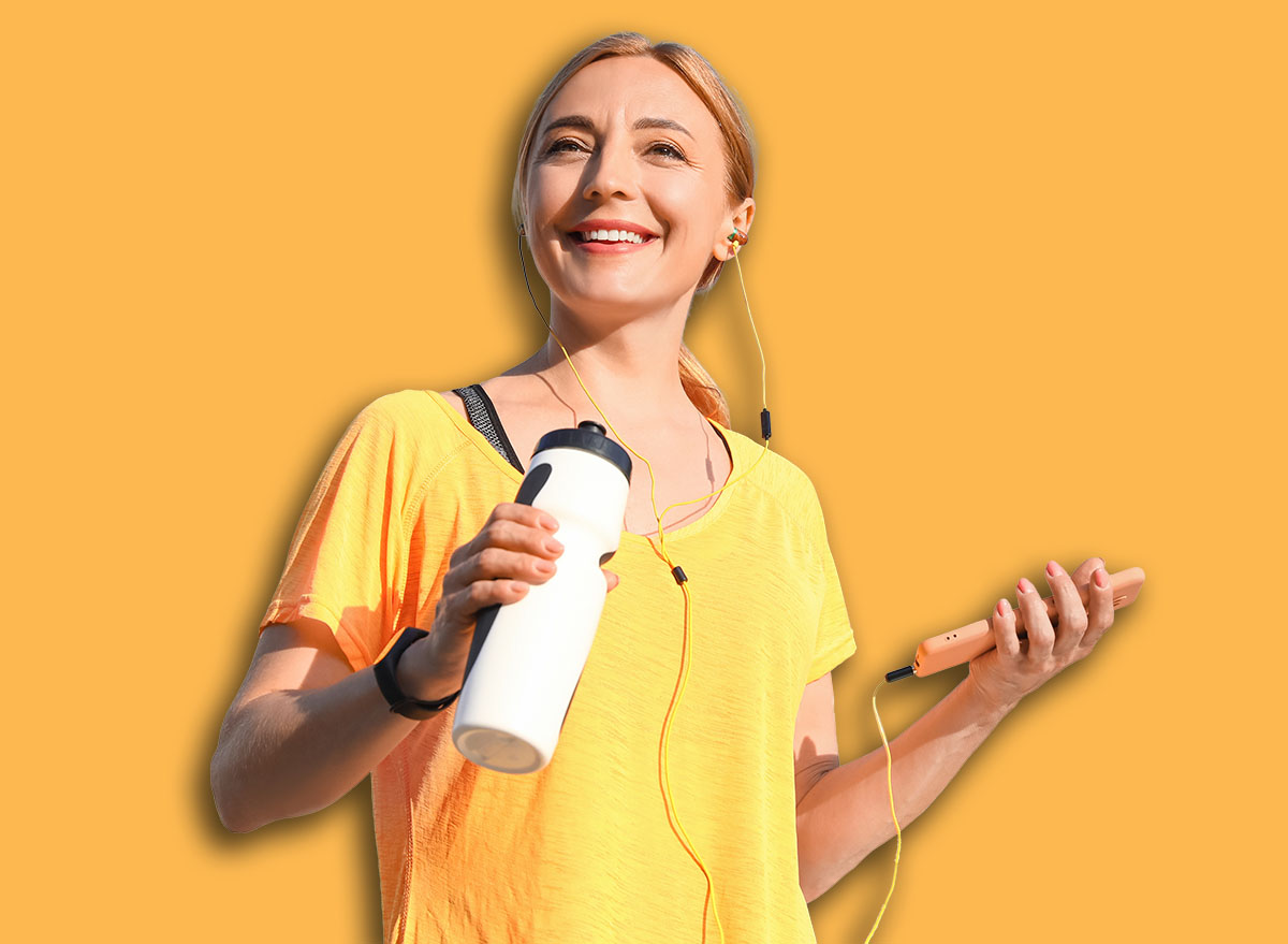 Sporty mature woman with bottle of water listening to music outdoors