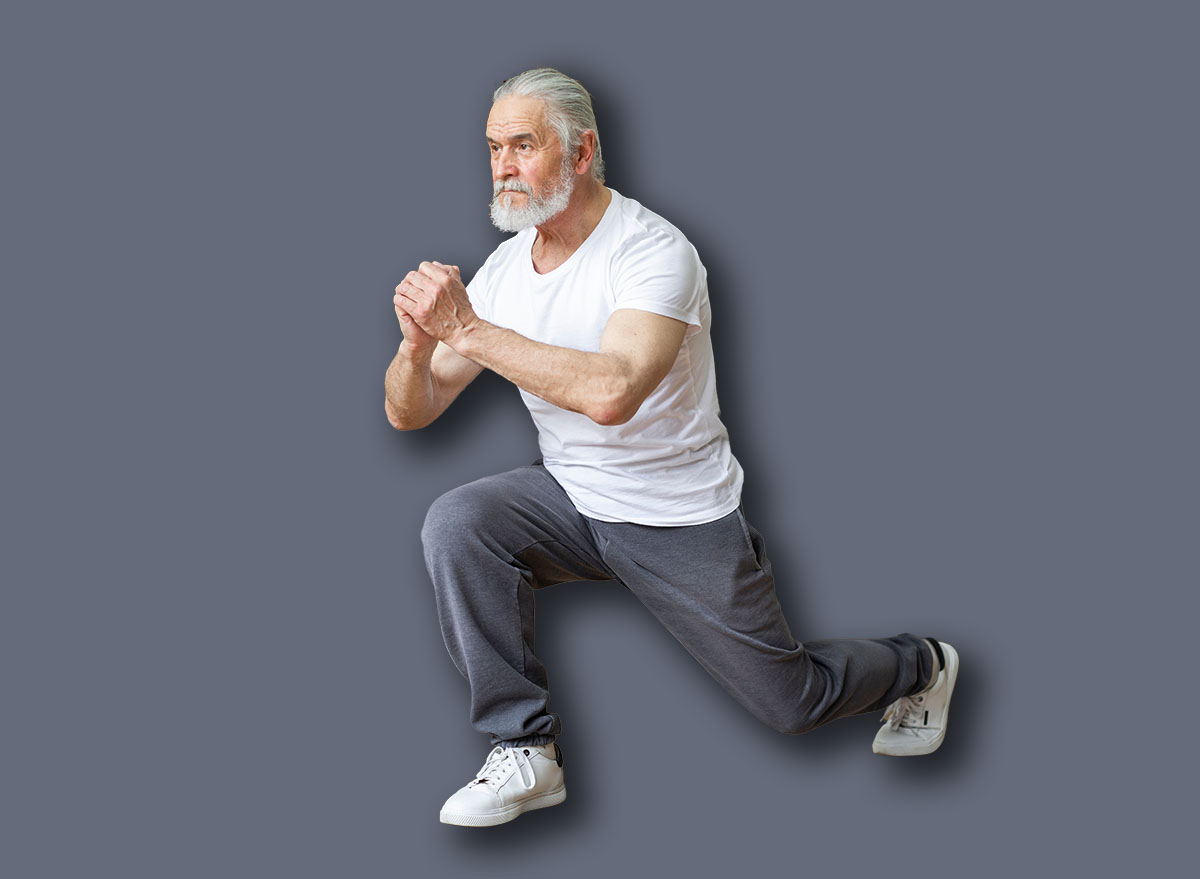Motivated athletic senior man in sportswear and sneakers doing lunges at home, looking at copy space. Good-looking grandfather exercising in living room while coronavirus pandemic, full length shot