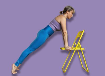 A woman leading a healthy lifestyle and doing yoga, performs Chaturanga Dandasana exercise with a chair, plank pose, trains in a fitness center in sportswear, in full growth