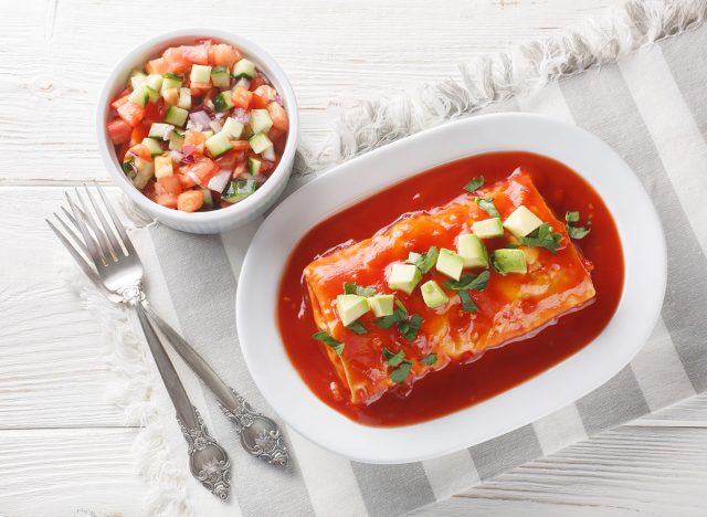 Tasty Wet Burritos with a beef, rice and refried bean filling wrapped in a tortilla smothered with red sauce closeup on the plate on the wooden table. Horizontal top view from above