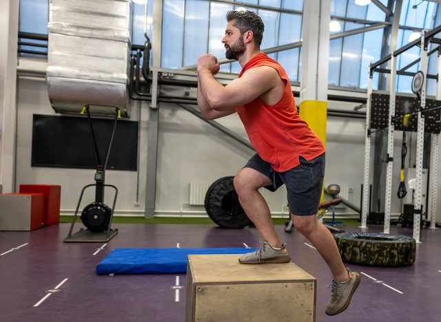 Man in sportswear doing step up workout with wooden box in crossfit gym.