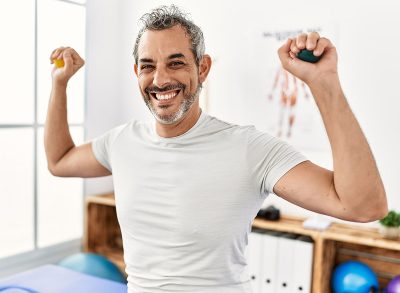 Middle age grey-haired man patient having rehab press balls with hands at rehab clinic
