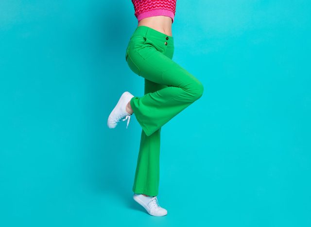 Cropped photo of half body slender girl legs dressed green retro pants standing on one feet tiptoe isolated on blue color background