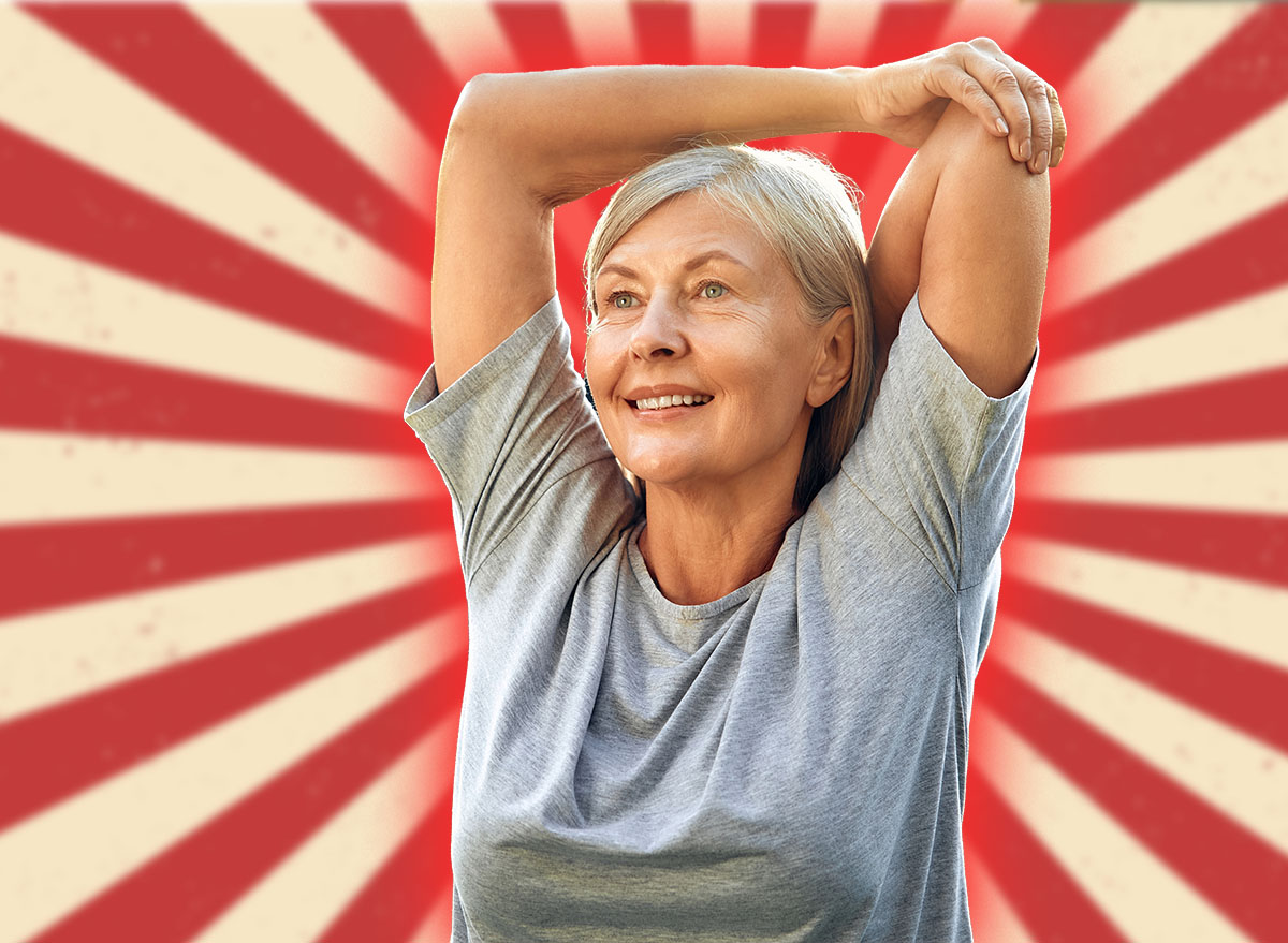 A joyful senior woman is gracefully stretching her arms outdoors in a lush, expansive green park, fully embracing a life of wellness, vitality, and the beauty of nature around her