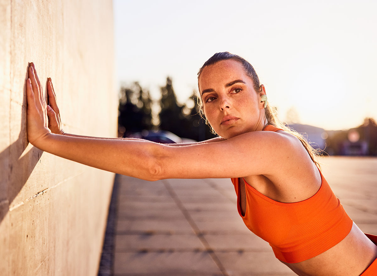 Focused woman in orange sports top leaning against a wall exercising outdoors