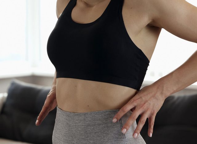 Young woman has workout at home during quarantine. Stand alone and show beautiful amazing abs muscles on her body. Pull training pant out. Slim fit and powerful woman's body.