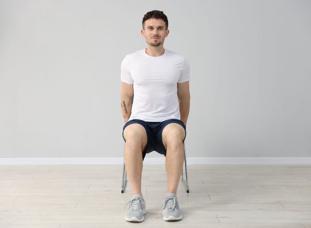 Handsome man exercising with chair at home