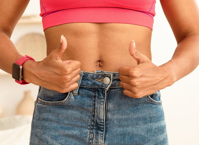Successful Weight Loss. Black Woman With Flat Muscular Belly Gesturing Thumbs Up After Slimming, Showing Perfect Abs Standing Indoors. Weight-Loss And Fitness Training Motivation. Cropped