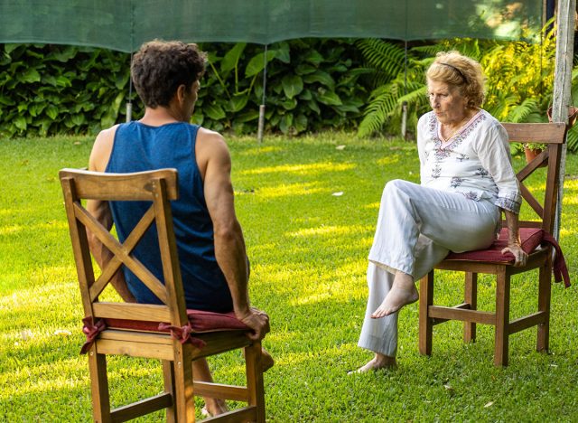 Senior woman and her physiotherapist are sitting on chairs in a garden, practicing rehabilitation exercises to improve mobility and well-being