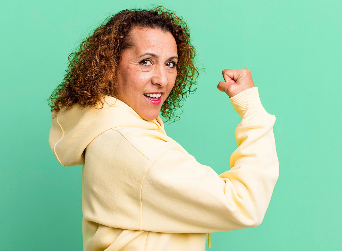 middle age hispanic woman feeling happy, satisfied and powerful, flexing fit and muscular biceps, looking strong after the gym