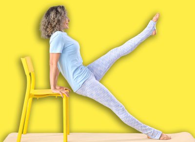 Sporty mature woman doing yoga with chair on mat against light background