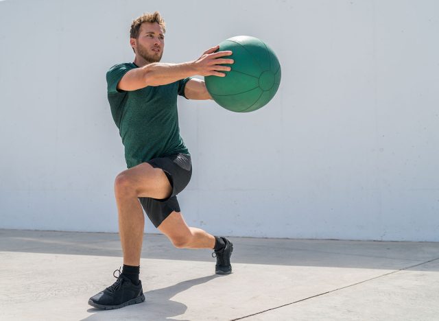 Working out man training legs and core ab workout doing lunge twist exercise with medicine ball weight. Gym athlete doing lunges and torso rotations for abs training.