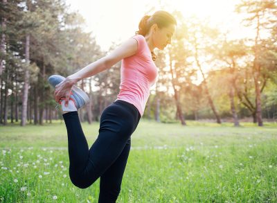 Fitness woman streching leg in sunset park