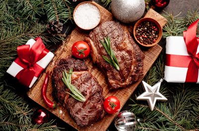 Christmas dinner for two, grilled beef steak, ribeye, greens and spices on a stone table with a Christmas tree and New Year's toys