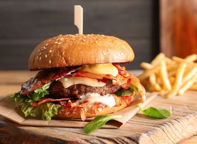 Tasty burger with bacon and french fries on wooden board