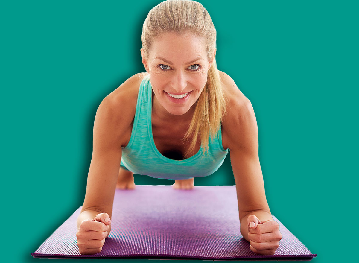 Portrait shot of attractive middle aged woman doing plank exercises on yoga mat in the fitness studio.