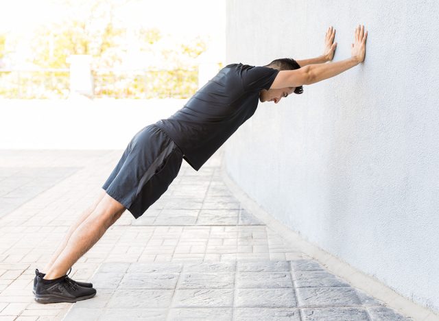 Profile shot of focused man in sportswear pushing wall on footpath in city