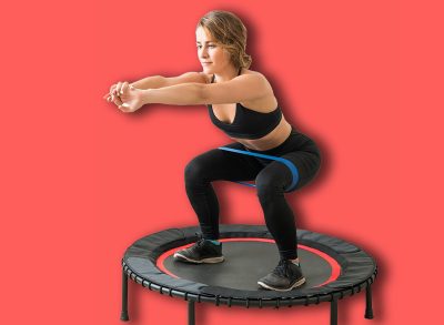 Confident slim female doing squats with resistance band on trampoline during high intensity interval training at studio