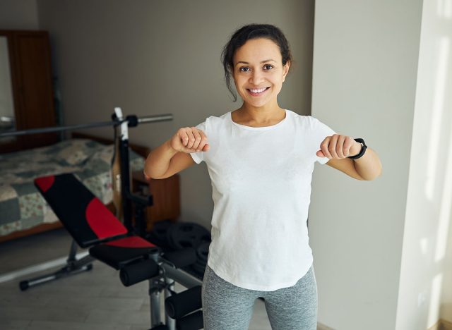 Smiling beautiful young dark-haired Caucasian fit woman doing a standing stretching exercise with bent elbows