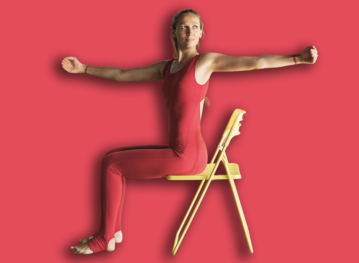Woman practicing yoga therapy, performs a lateral twist while sitting on a chair in the studio