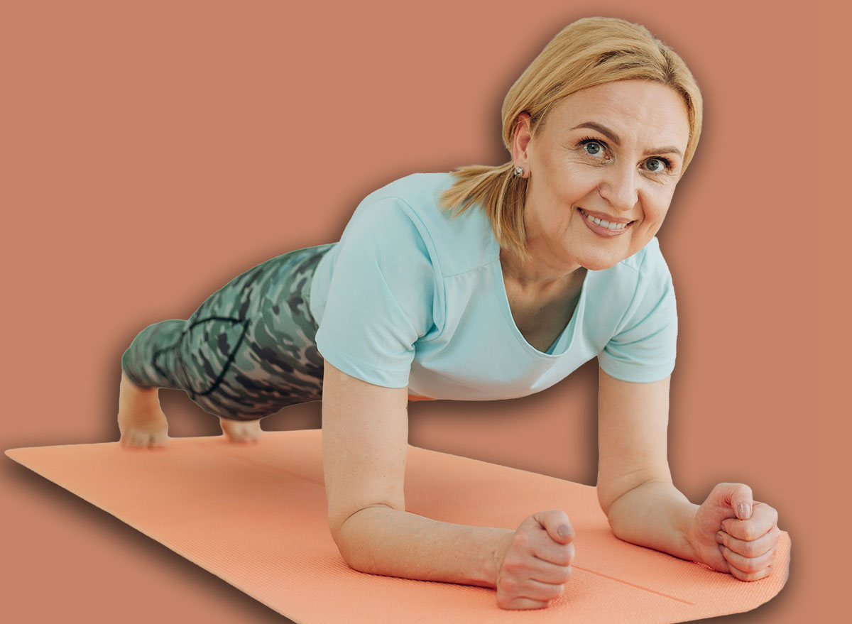 Sporty middle-aged caucasian woman standing in plank position using laptop for training at home