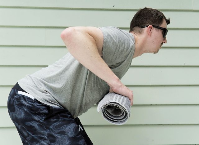 Man doing bend-over rows with a towel. This exercise is also called "towel rows." He is exercising outdoors.