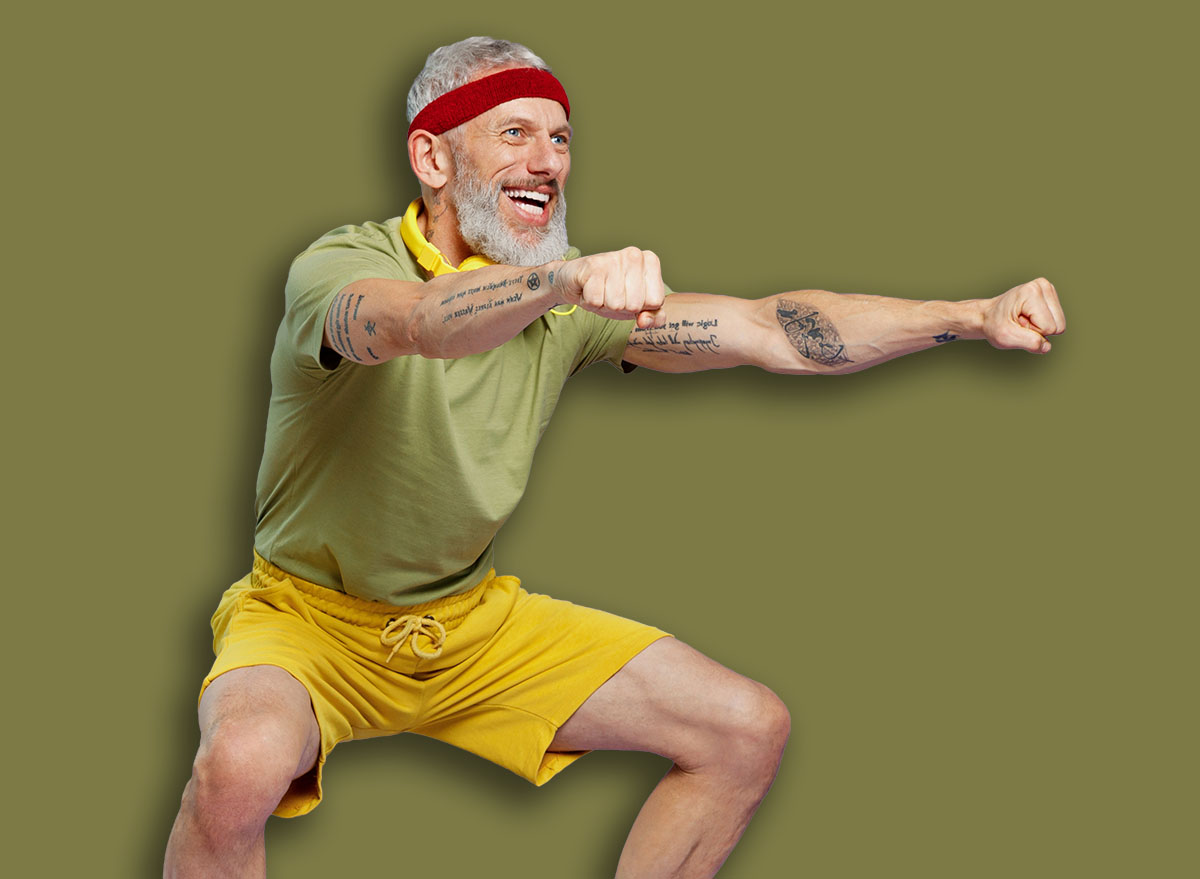 Full size body length fitness vivid elderly gray-haired bearded man 40s years old in headband khaki t-shirt look aside doing side squat isolated on plain pastel light purple background studio portrait