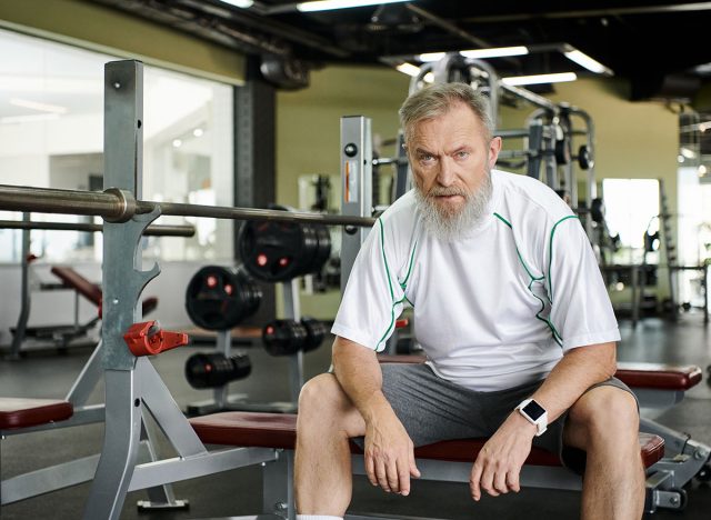 tired elderly man with beard looking at camera after workout, exercise machine in gym, athlete