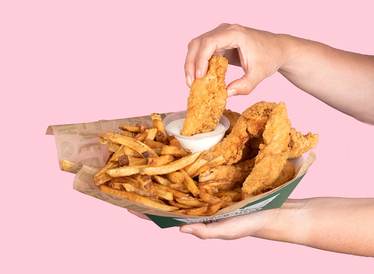 Hand holding basket of chicken tenders and fries