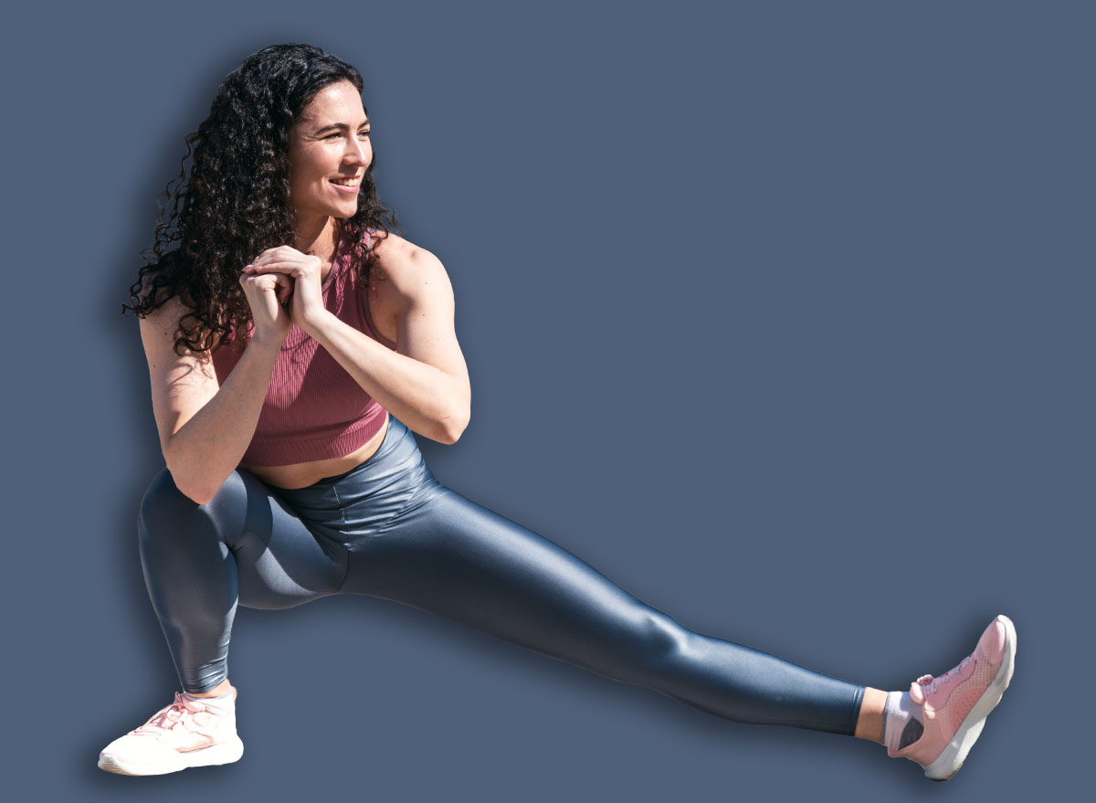 Young smiling fit woman doing stretching exercises for legs before training. Female athlete preparing for jogging outdoors. Runner doing side lunges. Active lifestyle concept.