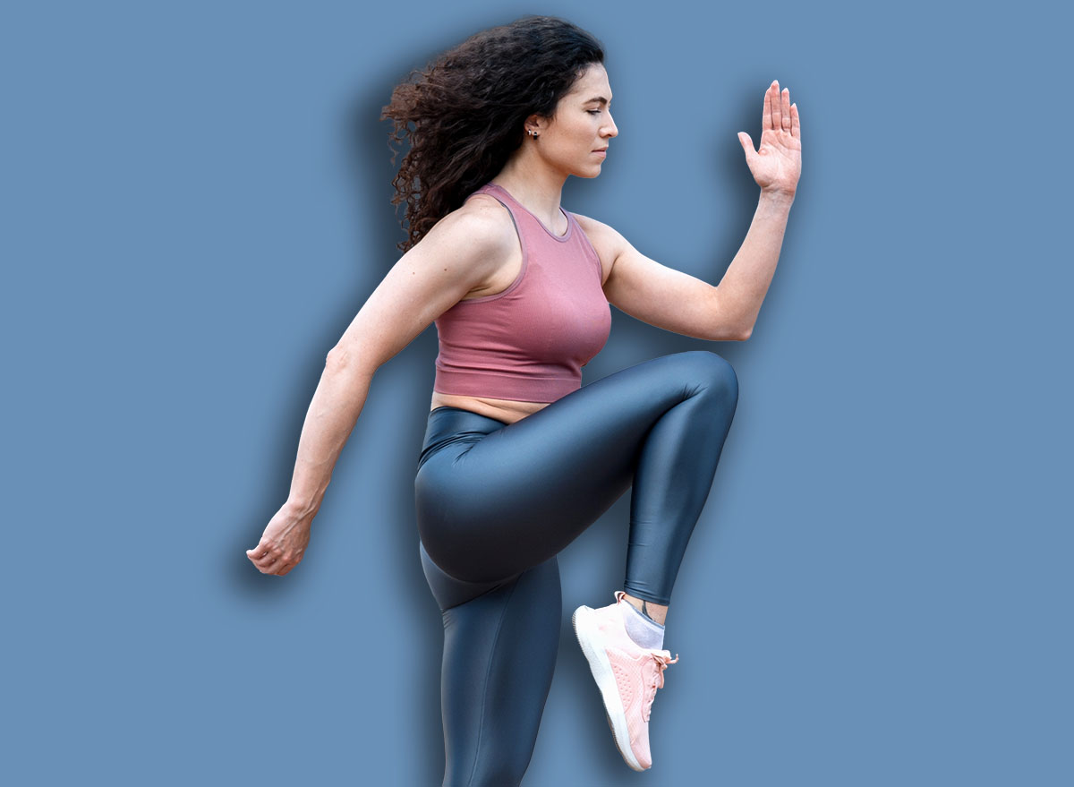 Warm-up, doing cardio workout outdoor. Sporty young woman in sportswear standing on one leg and touching knee with elbow, doing high knees exercise on street.