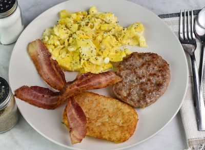 scramble eggs top with parsley served ith hash browns sausage patty and bacon,