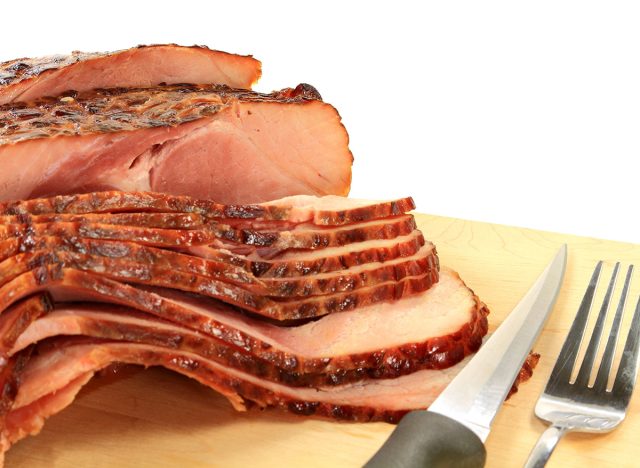 Close-up view Finally backed pre cooked smoked Spiral-cut of Pork Ham over wooden cutting board ready to arrange American South Traditional New Years Day meal over white background