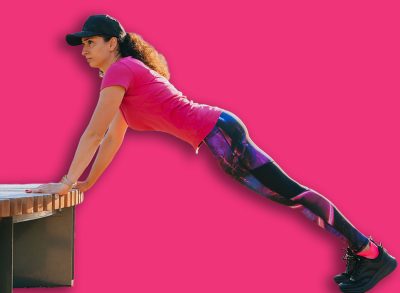 Woman doing incline push-ups on a bench in an outdoor gym, focusing on strength and endurance during her fitness routine in an urban park