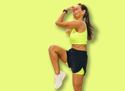 A woman performs a high-knee exercise on a waterfront promenade, enjoying the sunny day and the sea breeze.