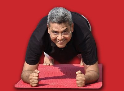 Senior Indian man doing forearm plank on a yoga mat outdoors, smiling and enjoying his fitness routine in the fresh morning air at Riverfront, Ahmedabad. Man is staying fit after 60 years of age.