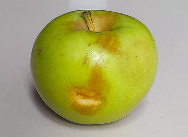 A whole green apple with brown, sunken areas, likely bruising or early spoilage.
