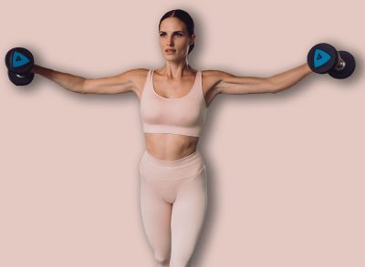 Fit woman holding dumbbells extended outward during lateral raise, showcasing full-body engagement, arm activation, and disciplined strength movement in modern gym.