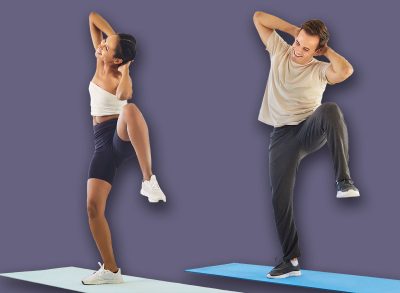 Happy couple doing home fitness workout together. Young fit woman and man perform exercise lifting knees up and to side with arms folded above head, two smiling active people training indoors