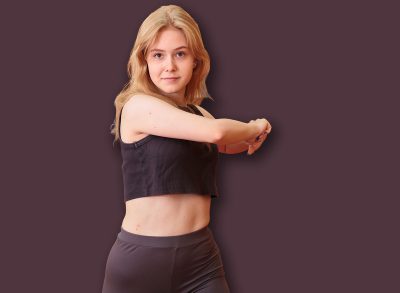 Fit woman doing standing torso twist stretch with arms extended during indoor warm-up