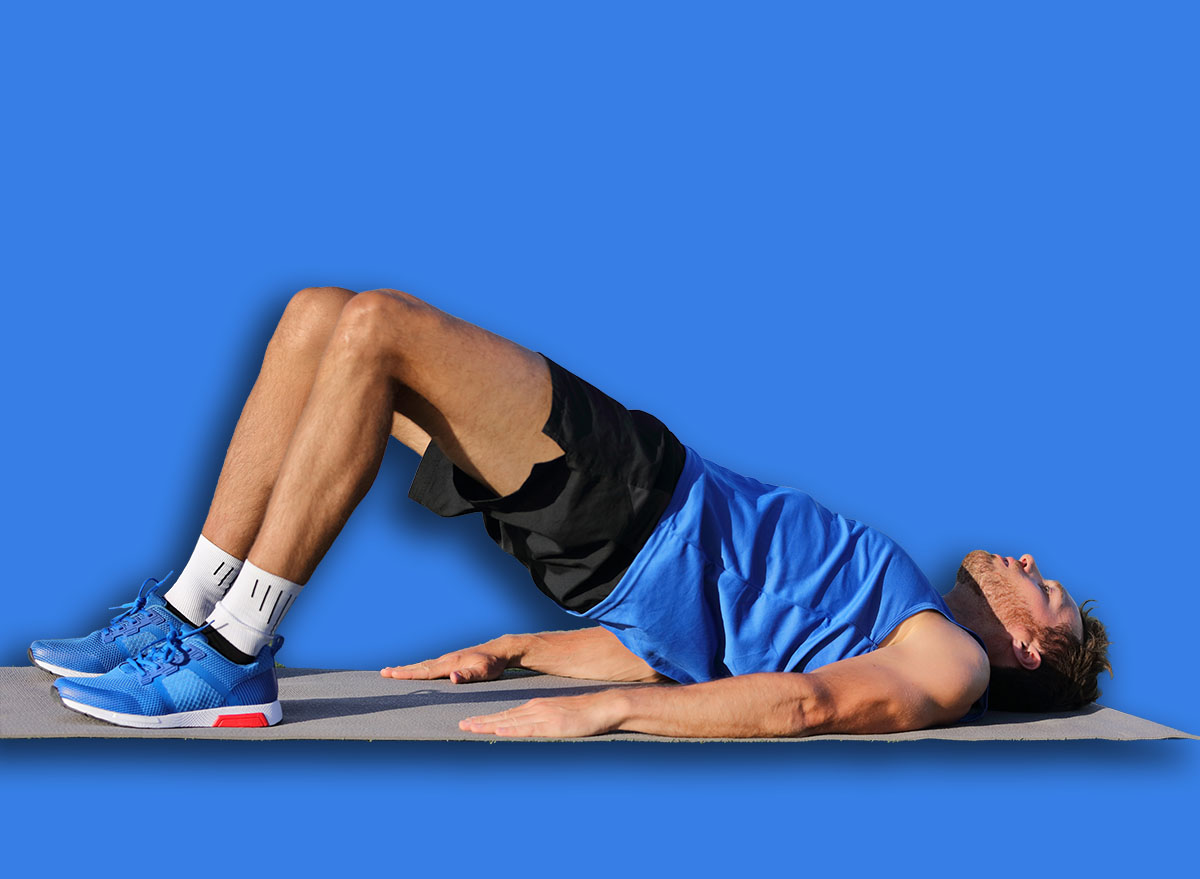 Fitness man doing bodyweight glute floor bridge pose yoga exercise. Fit athlete exercising glutes muscles with butt raise at summer outdoor gym instruction class on grass.