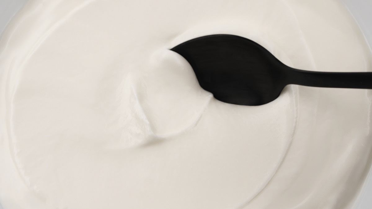 Close-up of a black spoon dipping into thick white yogurt or cream. Smooth dairy texture and fresh food concept. Minimal background for culinary, nutrition or healthy eating themes