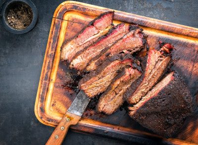 Traditional smoked barbecue wagyu beef brisket as piece and sliced offered as top view on an old cutting board with copy space left