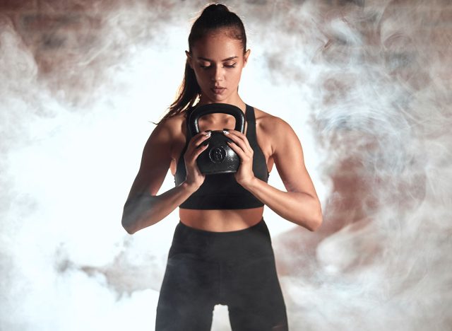 Young caucasian woman stand holding kettlebell in two hands. Steam background