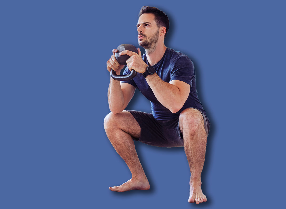 Training at home, young man doing squats with kettlebell weights.