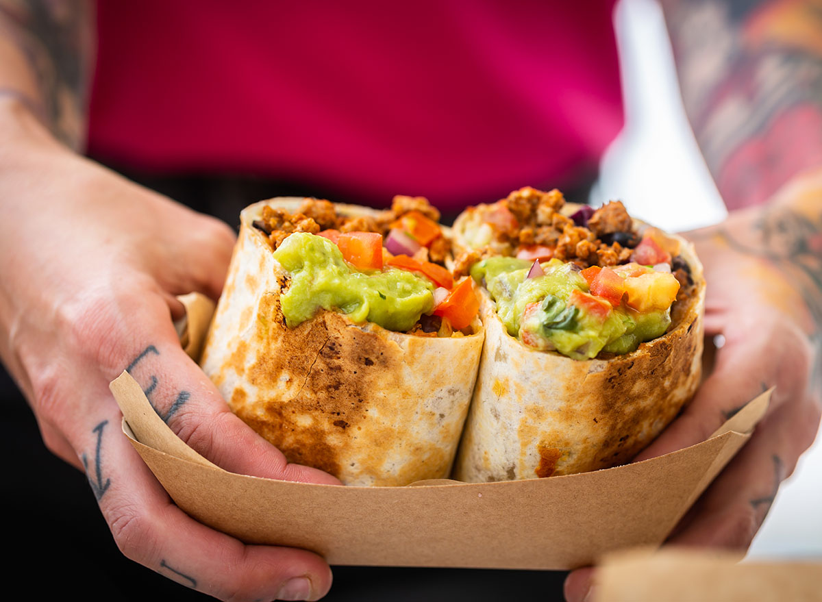 The male hands of a chef in a fast food cafe hold a burrito with minced meat and salsa and guacamole. Traditional Mexican dish