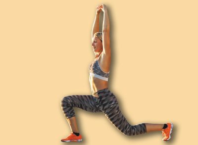 Adult woman lunges while holding arms above her head and warming up for sports training near the sea beach.