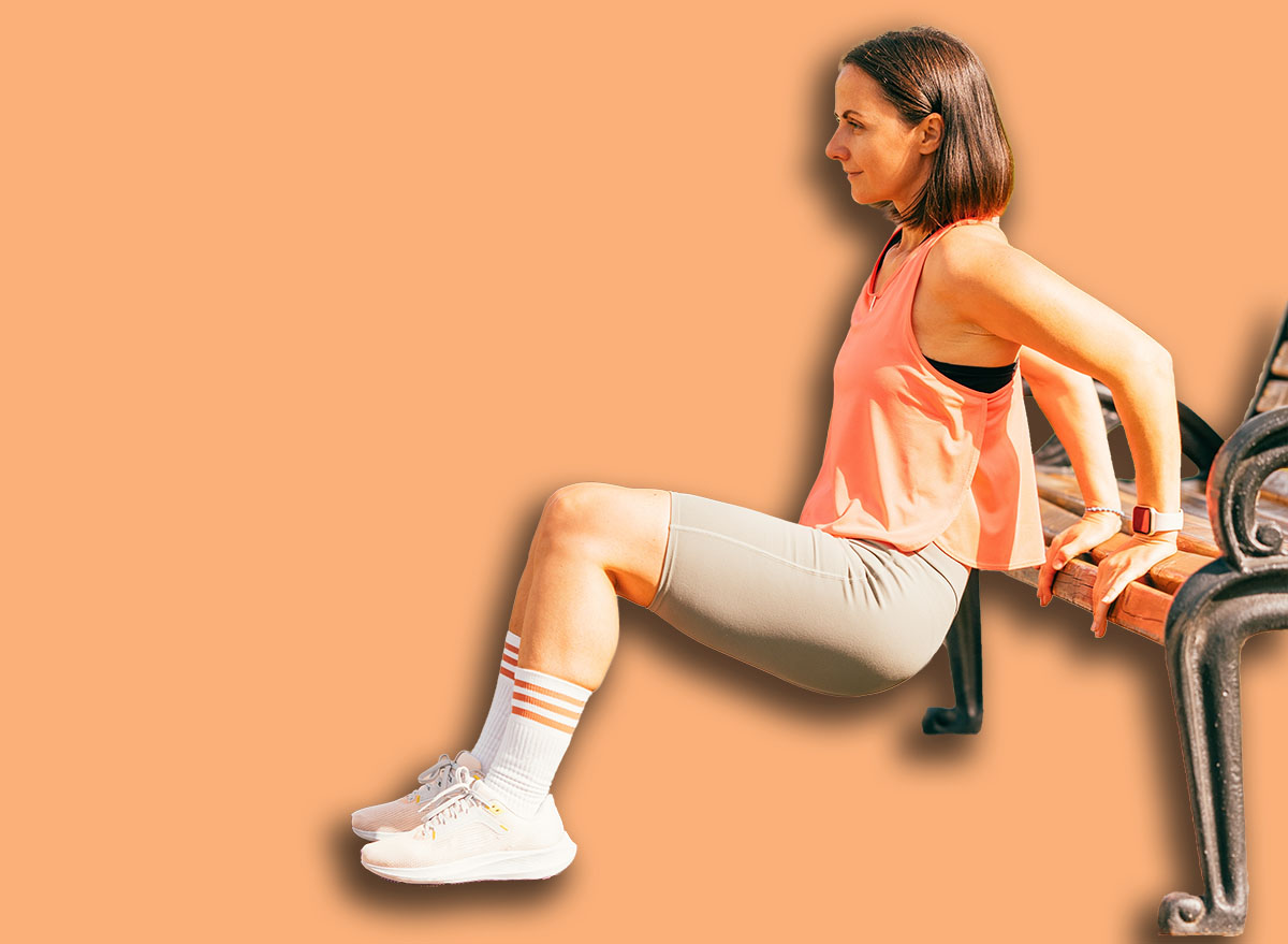 Vertical outdoors shot of a fit woman exercising her triceps on a park bench.