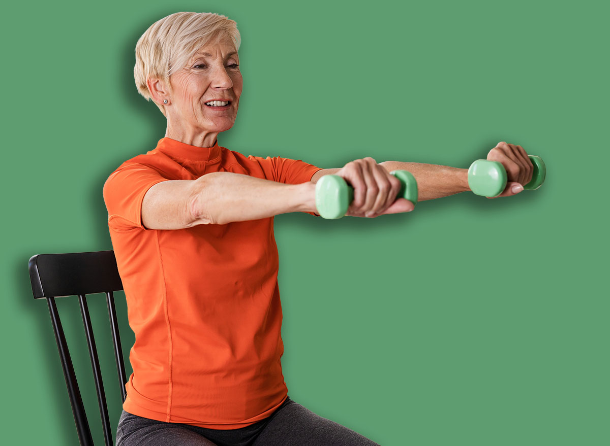 Smiling beautiful senior woman health instructor doing chair exercises with dumbbells