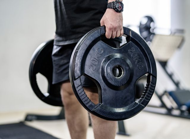 A man is holding a weight plate that is 20 kg. He is in a gym setting. Concept of strength and fitness, as the man is lifting a heavy weight.